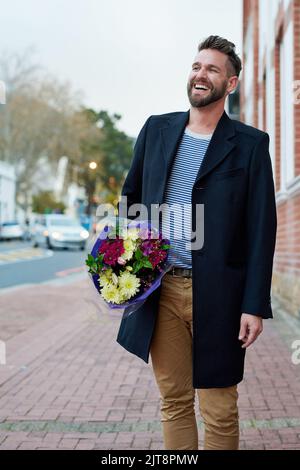 Ein hübscher junger Mann, der mit einem Blumenstrauß in der Hand durch die Stadt läuft. Stockfoto