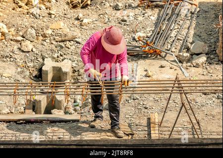 Ein Bauarbeiter verteilt ebenfalls geschlossene Stahlstäbe entlang der Länge der verformten Stäbe und bindet sie mit Stahldrähten zusammen. Stockfoto