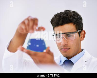 Der Höhepunkt des langen Experimentierens. Ein Labortechniker untersucht einen Becher aus blauer Flüssigkeit, während er im Labor steht. Stockfoto