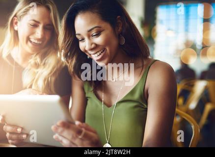 Die Freundinnen teilen sich etwas auf einem digitalen Tablet, während sie in einem Café sitzen. Stockfoto