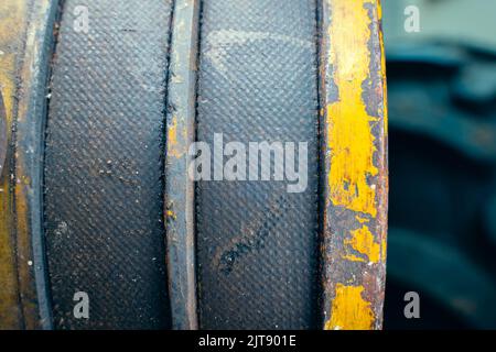 Zwei dicke Riemen am Motor in Nahaufnahme. Antriebsriemen alt abgenutzt an gelber Riemenscheibe, unscharfer Hintergrund. Industrieartikel in der Landwirtschaft Stockfoto