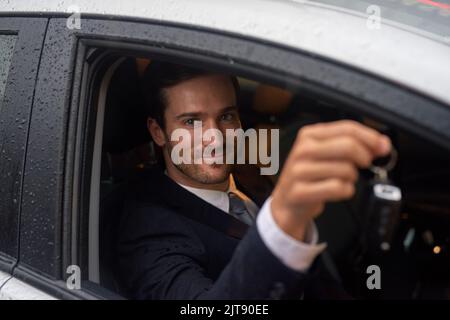 IVE arbeitete hart für diesen Moment. Ein lächelnder Geschäftsmann mit Schlüsseln, während er in seinem neuen Auto saß. Stockfoto