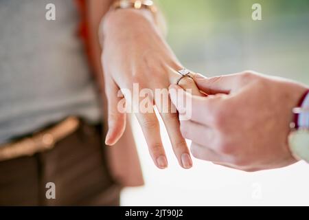 Sie sagte ja. Nahaufnahme eines Mannes, der einen Verlobungsring auf den Finger seiner Verlobten legt. Stockfoto