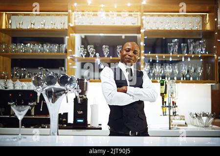 Herr seiner Domäne. Ein gut gekleideter Barkeeper, der hinter dem Tresen steht. Stockfoto