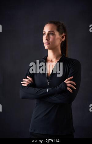 Fitness wird ernst. Studioaufnahme einer jungen Frau in Turnkleidung, die mit gekreuzten Armen vor dunklem Hintergrund steht. Stockfoto