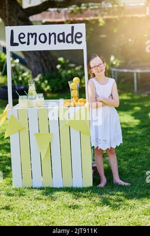 Bereit für das Geschäft. Porträt eines kleinen Mädchens, das Limonade von ihrem Stand draußen verkauft. Stockfoto