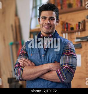 Ich bin zuversichtlich in meine DIY-Fähigkeiten. Porträt eines glücklichen Handwerkers, der mit gefalteten Armen in seiner Werkstatt steht. Stockfoto