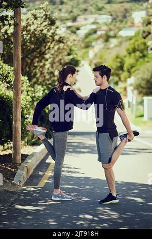 Sich gegenseitig unterstützen. Ganzkörperaufnahme von zwei jungen Menschen, die sich vor dem Training im Freien aufwärmen. Stockfoto