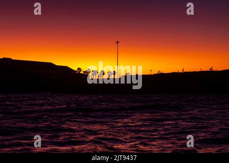 Palmen scherten sich scharf gegen die kräftigen orangen und rosafarbenen Farben eines Sonnenuntergangshimmels Stockfoto