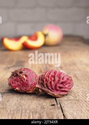 Nahaufnahme von Pfirsichgruben auf einem rustikalen Gartentisch, Landwirtschaftskonzept, frische Bio-Pfirsiche im Hintergrund Stockfoto