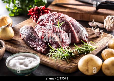 Rohes Fleisch in Form von Rinderschenkel, fertig zum Kochen mit Zwiebeln, Kräutern, Gewürzen, Knoblauch und Kartoffeln. Stockfoto