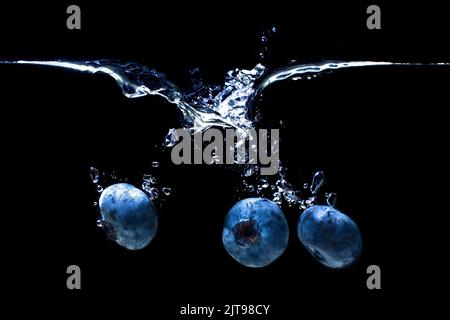 Blaubeeren sinken unter Wasser mit Luftblasen und Spritzern isoliert auf schwarzem Hintergrund. Stockfoto
