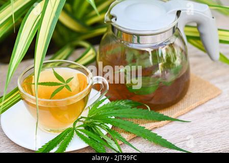 Cannabis Tee Kräuter auf Teetasse und Glaskanne mit Cannabisblatt Marihuana Blätter Kraut auf Natur Hintergrund, Gesundheit Tee mit Hanfblatt Pflanze THC CBD HE Stockfoto