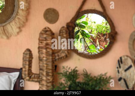 Ein stilvolles und modernes Boho-Interieur des Wohnzimmers mit einem Spiegel, einer Kaktusstatue und einer Pflanze. Stockfoto