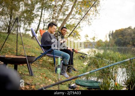 Mann im Gespräch mit männlichen Freunden beim Fischen in der Natur Stockfoto