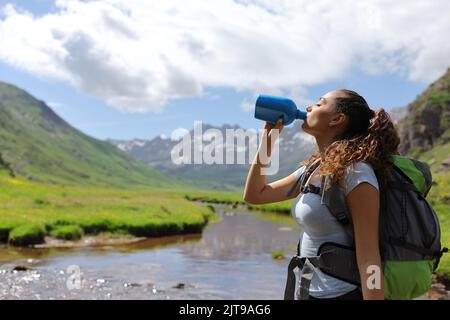 Profil eines Wanderers, der Wasser aus der Kantine im Fluss im Berg trinkt Stockfoto