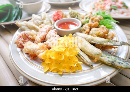 Frittierte, essbare tropische Blumen, Blätter und Gemüse, serviert auf einem weißen Teller, liegen flach auf dem Bambustisch. Gesunde Ernährung. Draufsicht. Nahaufnahme. Stockfoto