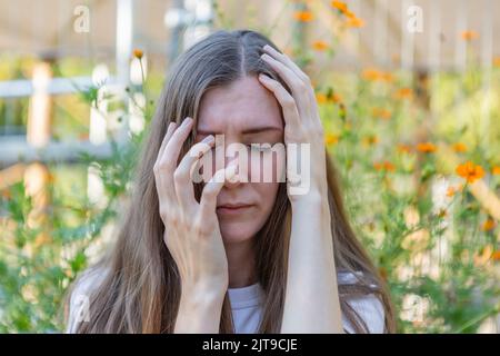 Eine Frau bedeckt ihr Gesicht mit ihren Händen, ihre Augen sind geschlossen Stockfoto