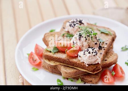 Sandwiches der Saison mit Sauerteig, Tomaten, Kräutern, Quinoa und veganer Sause. Gesundes veganes Frühstück. Stockfoto