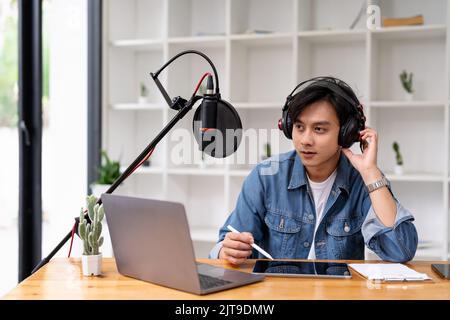 Asiatischer Mann, der einen Podcast auf einem Laptop mit Mikrofon aufzeichnete, während er zu Hause Live-Streaming online hatte Stockfoto