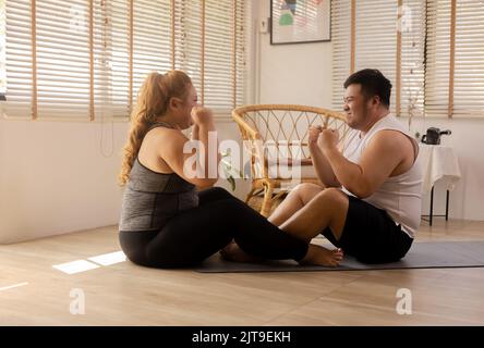 Junge asiatische mollige Paar trainieren und arbeiten zusammen im Wohnzimmer zu Hause. Plus Size Mann und Frau jubeln und zeigen positive Energie und ermutigen sich gegenseitig, dass sie es tun können Stockfoto