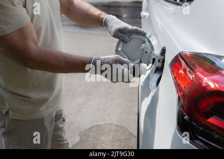 Mann öffnet Mann öffnet die Luke des Gastanks des Autos. Mann, der die Kappe des Gastanks abschraubt Stockfoto