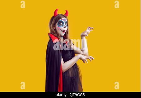 Erstaunt Frau gekleidet als verrückter Teufel mit schrecklichen Make-up-Shows, um Platz auf gelbem Hintergrund zu kopieren. Stockfoto