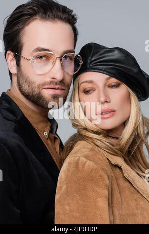 Portrait der blonden Frau in stilvoller Baskenmütze in der Nähe bärtiger Mann in Sonnenbrille auf grauem, Stock Bild isoliert Stockfoto