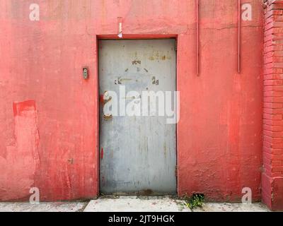 Blick auf eine alte, graue, geschlossene Tür an einer roten Wand Stockfoto