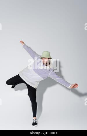 In voller Länge von jungen Mann in stilvollen sportlichen Outfit und panama-Hut posiert auf grau, Stock Bild Stockfoto