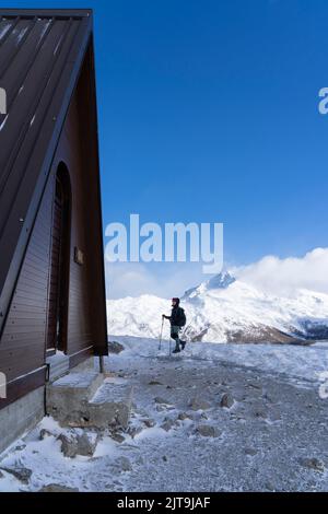 Eine vertikale Aufnahme eines kaukasischen Wanderers, das die Wanderstöcke mit verschneiten Bergen im Hintergrund hält Stockfoto