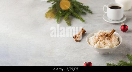 Skandinavischer Reisbrei mit Zimt in einer Schüssel, umgeben von Weihnachtskugeln. Frühstück am Heiligabend. Stockfoto