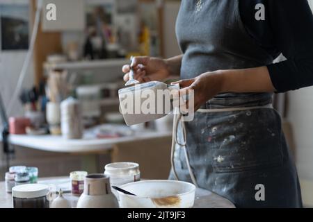 Crop Foto von Frau Handwerker Herstellung Steingut Vase Vorbereitung für die Farbe mit Pinsel Stockfoto