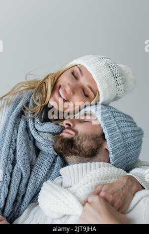 Happy blonde Frau in gestrickten Schal umarmt mit bärtigen Freund im Winter Hut isoliert auf grau, Stock Bild Stockfoto