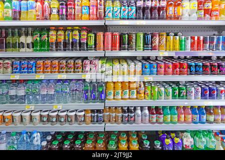 Reihen von bunten Softdrink-Dosen und -Flaschen einige zuckerhaltige, hohe Zuckergehalte und CO2 kohlensäurehaltige Getränke auf Regalen im Convenience-Shop Essex England UK Stockfoto