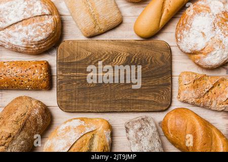 Minimalistisches Holz Schneidebrett blank mockup auf dem Hintergrund der Arten von hausgemachtem Brot. Verschiedene Arten von frischem Brot als Hintergrund, Blick von oben mit Spa Stockfoto