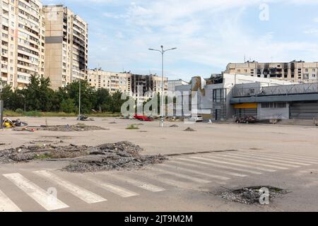 KHARKIV, UKRAINE - 30. Jul. 2022: Wohnhochhäuser mit Spuren von Bränden und Kratern durch Granatexplosionen. Umgedrehter Wagen. Die Straßen von Charkiw während des Krieges. Stockfoto