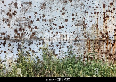 CHARKIW, UKRAINE - 30. Jul. 2022: Betonwand mit zahlreichen Spuren von Bruchstücken explodierender Muscheln. Die Straßen von Charkow während des Krieges mit der Russischen Föderation. Stockfoto