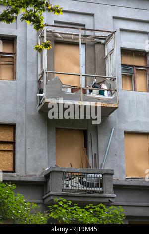 KHARKIV, UKRAINE - 30. Jul. 2022: Fragment der Fassade des Gebäudes mit Sperrholzfenstern anstelle von Glas. Charkiw während des Krieges mit der Russischen Föderation. Stockfoto