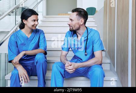 Gesundheitspersonal sitzt im Krankenhaus auf der Treppe und spricht während der Pause. Medizinisches Personal Stockfoto