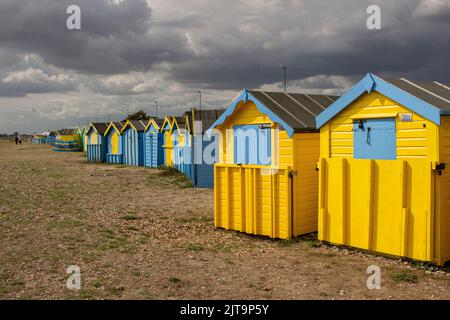 Strandhütten am East Beach, Littlehampton, West Sussex, Großbritannien; leuchtend gelb und blau gestrichen und gegen einen stürmischen Spätsommerhimmel gesehen Stockfoto