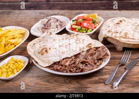 Fleisch Döner Kebab auf dem Teller. Türkischer Fleischspieß auf Holzhintergrund. Serviert mit heißem Lavasch. Traditionelle türkische Küche. Nahaufnahme Stockfoto