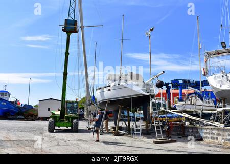 Kran, der einen Mast wieder auf ein Segelboot in East Llanion boatyard, East Llanion, Pembrokeshire, Wales, hebt Stockfoto