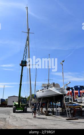 Kran, der einen Mast wieder auf ein Segelboot in East Llanion boatyard, East Llanion, Pembrokeshire, Wales, hebt Stockfoto