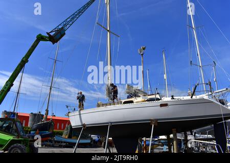 Kran, der einen Mast wieder auf ein Segelboot in East Llanion boatyard, East Llanion, Pembrokeshire, Wales, hebt Stockfoto