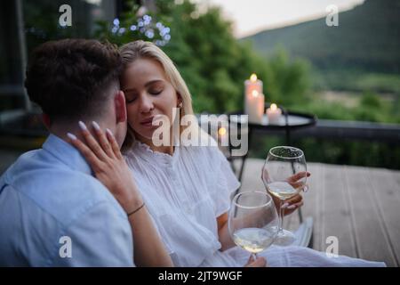 Junges Paar mit Wein ausruhen im Freien auf der Terrasse am Abend, Wochenende weg in winzigen Haus auf dem Land, nachhaltiges Leben. Stockfoto