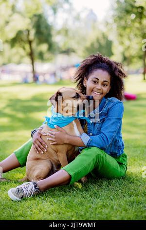 Multirassisches Mädchen, das mit ihrem Hund draußen im Park sitzt und sich ausruht, ihn trainiert und gemeinsam Freizeit verbringt. Konzept der Beziehung zwischen Stockfoto