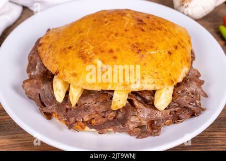 Fleisch zwischen Brötchen. Fleischspender im fetten Brot auf Holzhintergrund. Traditionelle türkische Küche. Nahaufnahme. Lokaler Name tombik et Doner Stockfoto