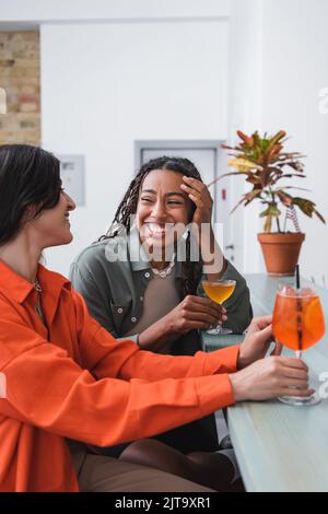 Glückliche afroamerikanische Frau, die Cocktail hält und ihre Freundin im Café ansieht, Stockbild Stockfoto