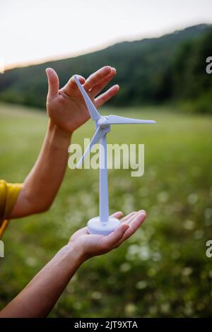 Nahaufnahme der Hände mit Modell des Windturibe in der Natur. Konzept der ökologischen Zukunft und nachwachsenden Ressourcen. Stockfoto